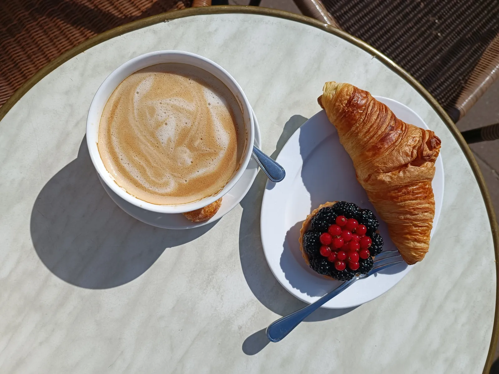Milchkaffee, Croissant und Beerentartelette auf einem Marmortisch