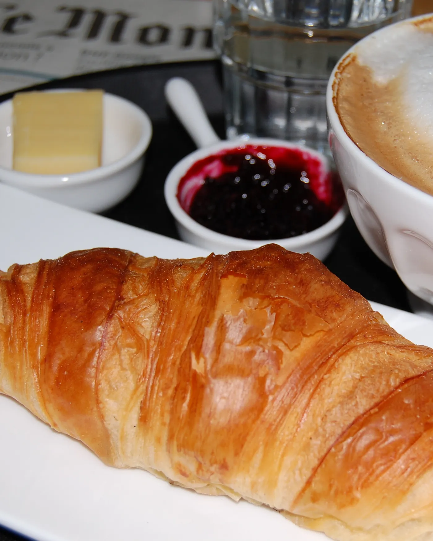 Croissant, Milchkaffee und Konfitüre auf einem Tablett